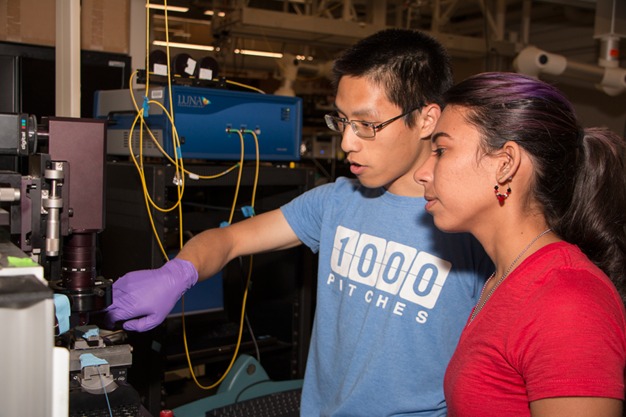 Department of Materials Science and Engineering graduate student Peter Su shows Summer Scholar Ashley Del Valle Morales how to operate a laser and detector system she will use during her summer project under Senior Research Scientist Anuradha Agarwal. The system combines an optical setup with a laser to drive light through an optical fiber into a sensor sample and collect light passed through reso...