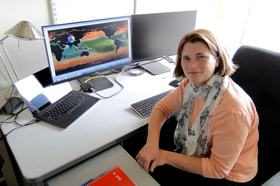 Stephanie Dutkiewicz in her office with a display of her phytoplankton model simulation