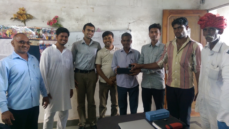 Pranay Jain (third from left) visits with the CEO of Maitree Dairy (second from left) and operators of Maitree's milk collection centers, dairy farmers, and other staff members in Dooni, Rajasthan, India. Jain visited them to better understand their needs, and to demonstrate the instrument he created to test milk quality. 