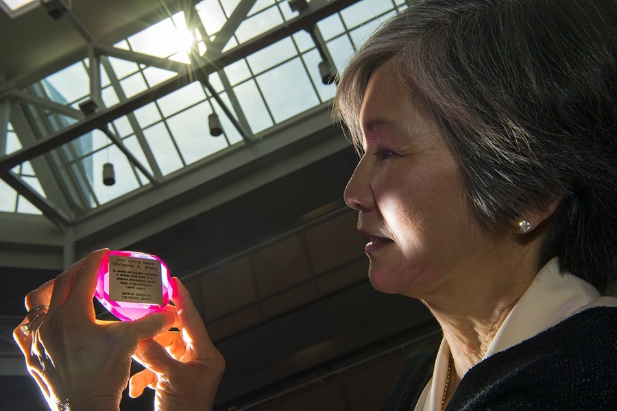 Christine Wang holds her American Association for Crystal Growth Award. Light catches the award, a synthetic ruby inset with a plaque describing the honor. 
