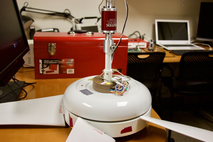 The base shown here contains the motor and the power electronics being tested. Mounted on the pole above are a dynamometer and sensors that measure torque (turning force) and thrust (forward force). Other instruments include a strobotac that monitors the speed at which the fan turns and a hot-wire anemometer that tracks the movement of the air.