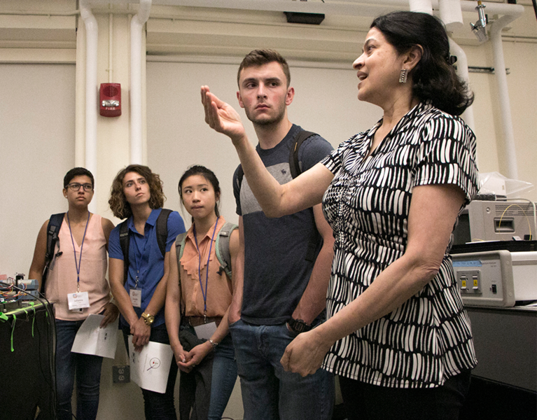 Principal Research Scientist Anuradha Agarwal (right) explains optical measurement equipment in her lab. Listening are (left to right) Julianna La Lane, Danielle Beatty, Sabrina Shen, and Michael Molinski.