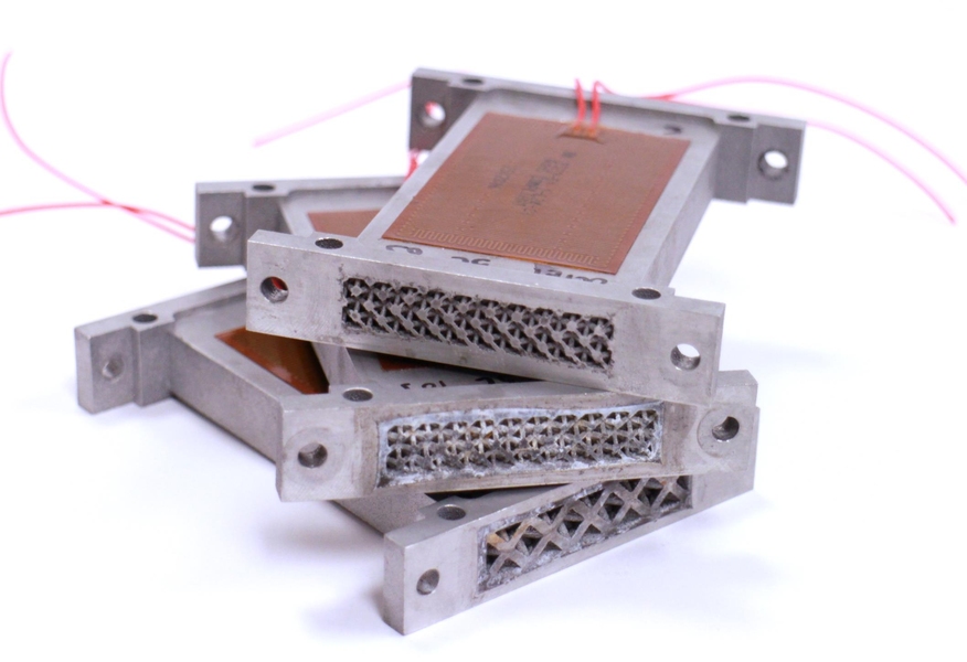 Additive manufacturing has enabled complex lattice forms to be built inside metal blocks that function both as heat exchangers and as structural components of the system. The inner geometry enhances the performance of the liquid-cooled system the exchanger serves.