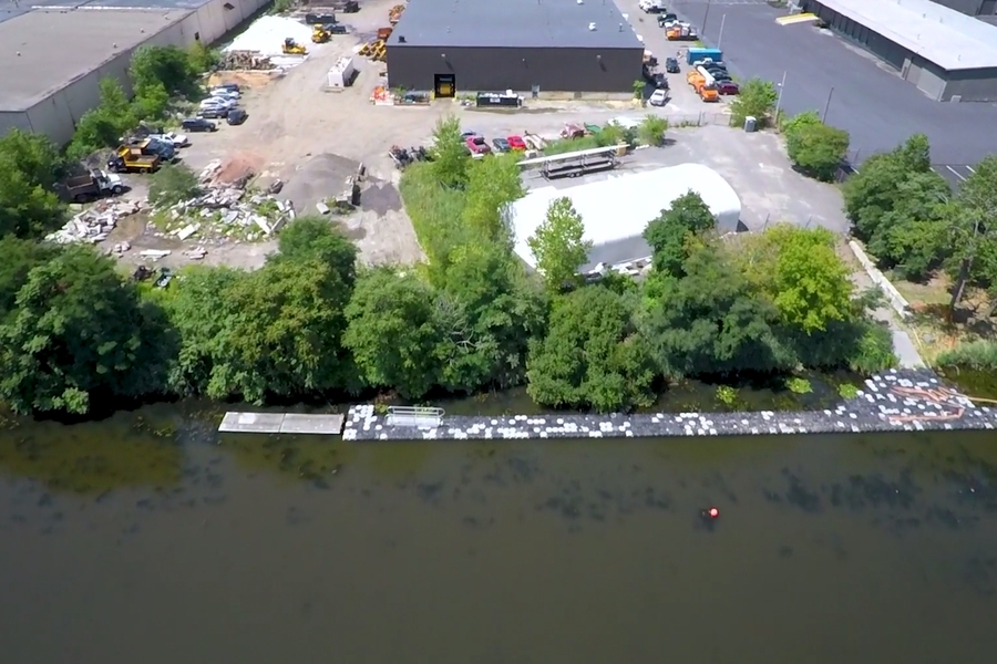 A proposed project site includes a 34,000-square-foot DPW office and garage, employee parking, a fuel station, and open-air materials and equipment areas, as well as a fabric-structure boat house at the river’s edge currently fenced off for use by a nearby school.