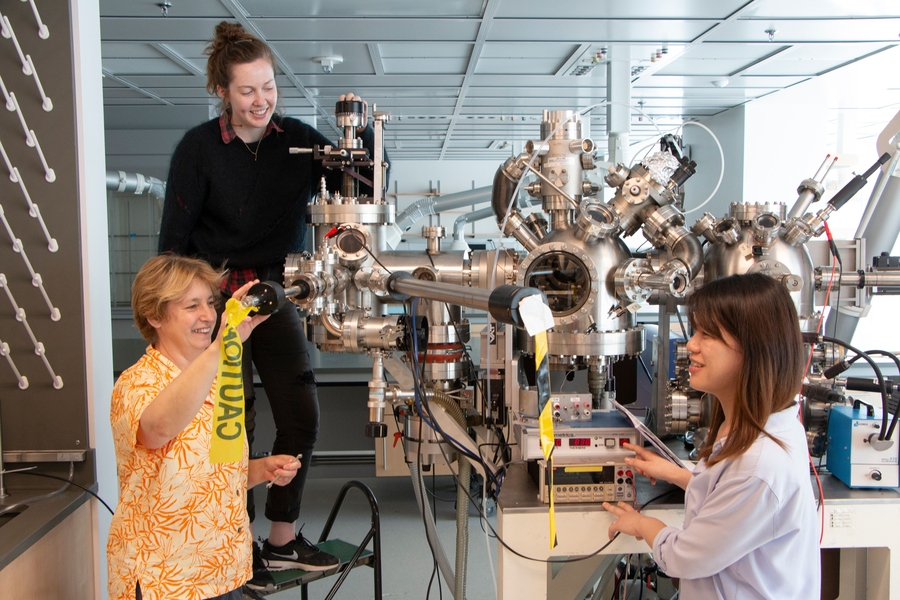 Professor Frances Ross (left), graduate student Kate Reidy (center), and postdoc Shu Fen Tan work together at the high vacuum evaporator chamber that is part of an electron microscopy suite donated to MIT by IBM.