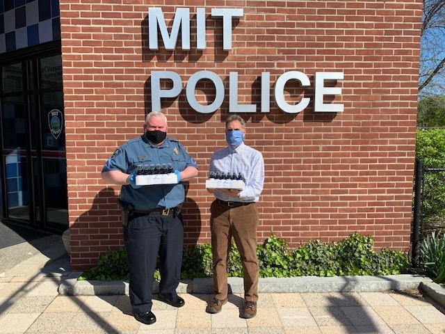Robert Edwards, associate director in EHS, hands off a donation of EHS "Everyday Hand Sanitizer" to MIT Police Sergeant David O’Conner.