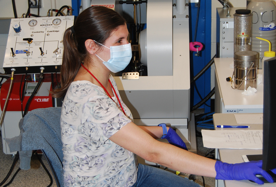 Postdoc Mary Andorfer stands in a lab with mask and gloves on.