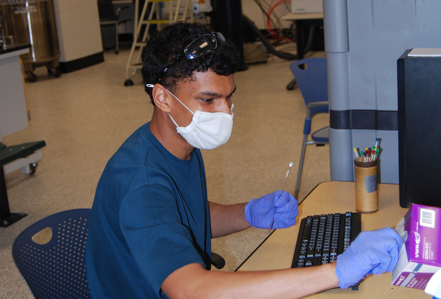 PhD student Tony Scott sitting at an instrument wearing mask and gloves