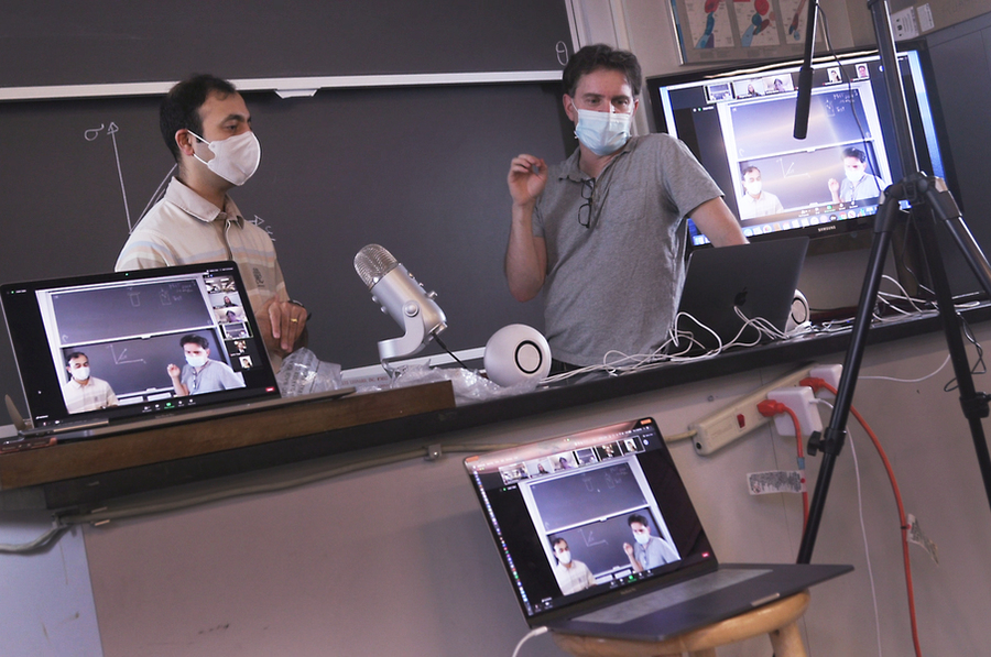 Rohit Karnik and Ken Kamrin, both wearing face masks, stand in front of a blackboard with laptop computers