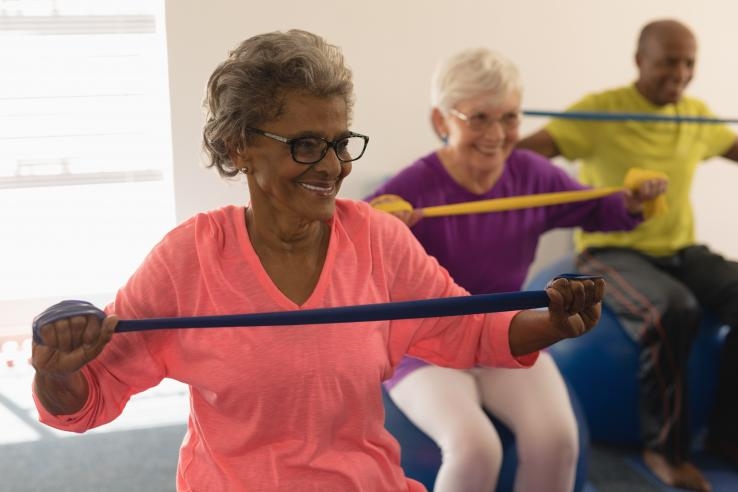 Photo of three smiling senior citizens exercising by stretching arm bands
