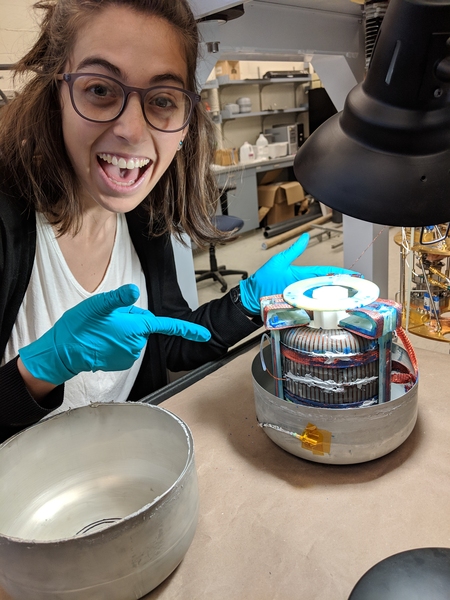 Photo of Chiara Salemi with blue latex gloves pointing at the ABRACADABRA toroid magnet