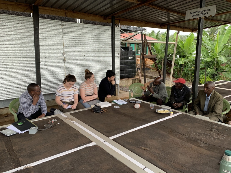 Photo of seven people sitting around a square table under an awning. 