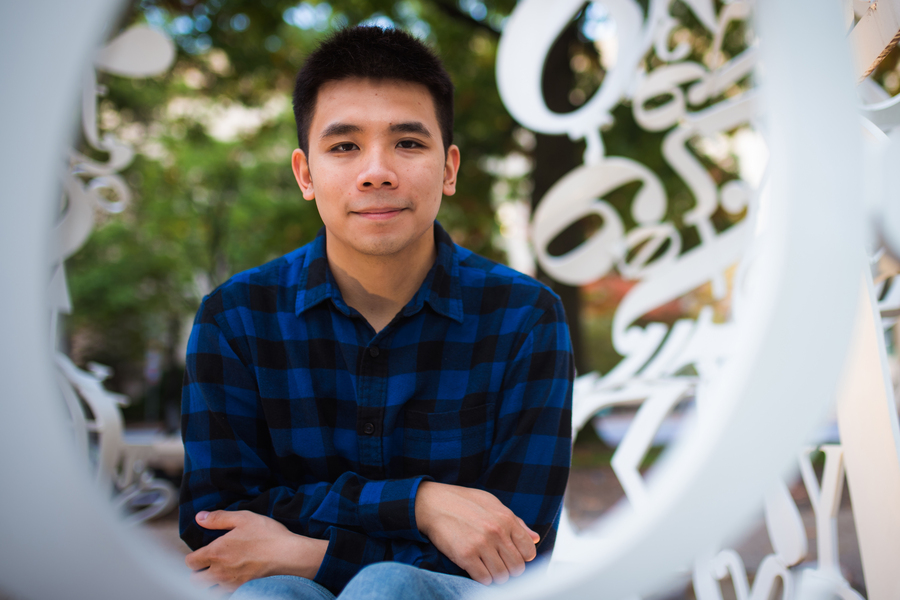 Photo of Thanh Nguyen posing by a white sculpture featuring white numbers and mathematical constants