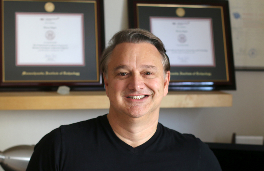 Photo of Renzo Zagni in front of two framed diplomas