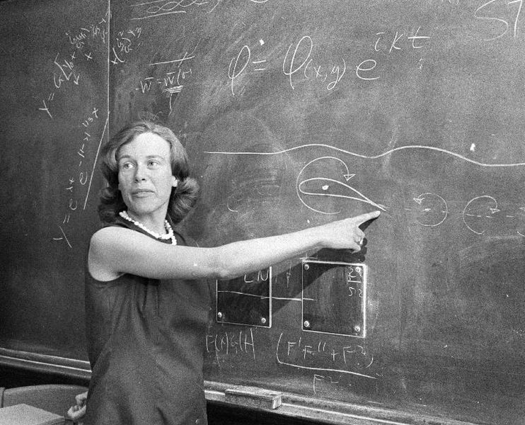 Black and white photo of a young Sheila Widnall pointing to a blackboard with equations on it