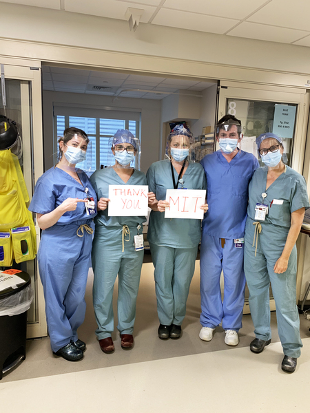 Photo of doctors wearing scrubs and an MIT-designed face shield holding a sign saying 