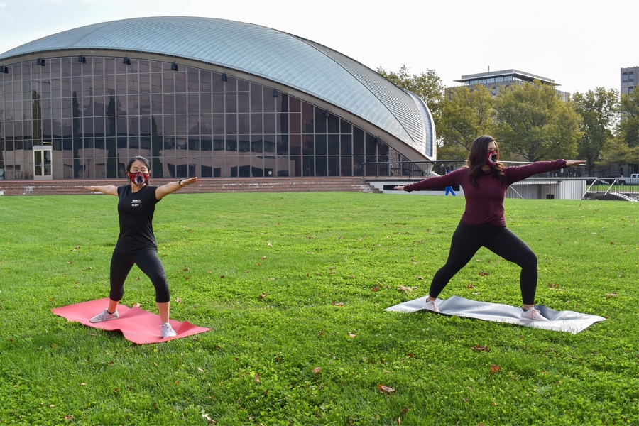 Photo of two women in face masks doing yoga outdoors on yoga mats.
