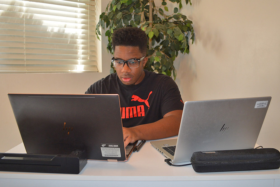 Xzavier Herbert sits at a table working on two laptops
