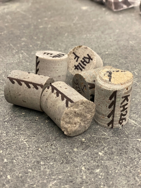 Photo of six gray cyllindrical rock core samples, each a few inches long, with markings in black marker along the outside