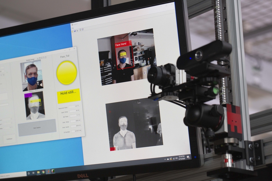 A thermal camera is pictured in front of a computer monitor with a person having their temperature scanned