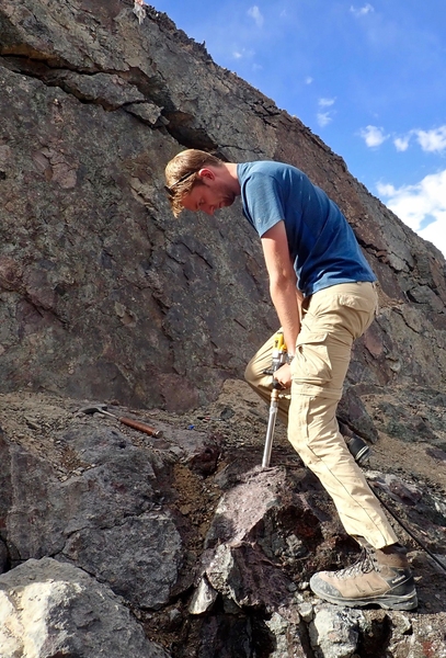 Photo of Craig Martin standing on the side of a rock formation, pressing a metal tube into the rock