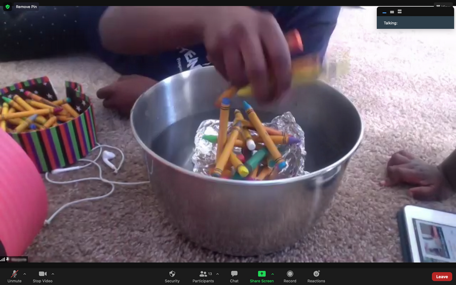 Zoom screenshot of a hand grasping crayons while hovering over a silver bowl filled with water.