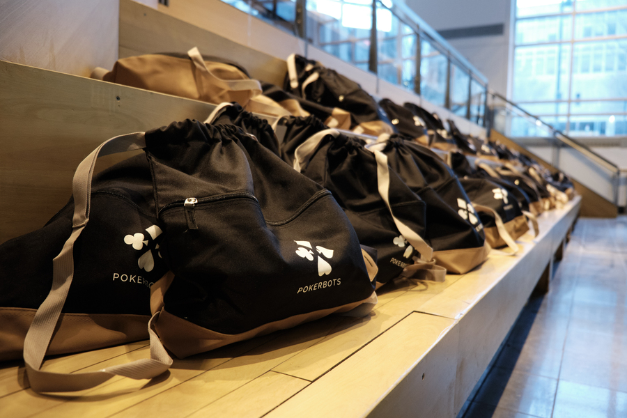 Photo of a row of gear bags, each embellished with the Pokerbots logo, lined up on a bench