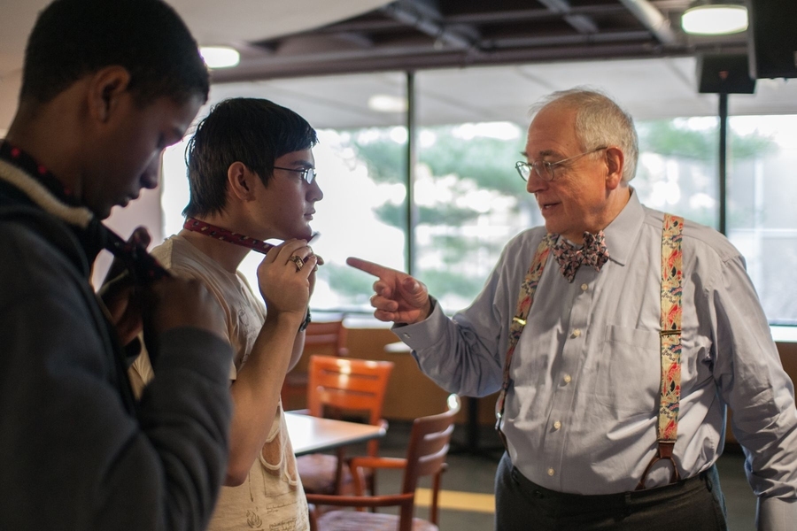 Photo of Bill Hecht teaching two young men how to tie a bow tie