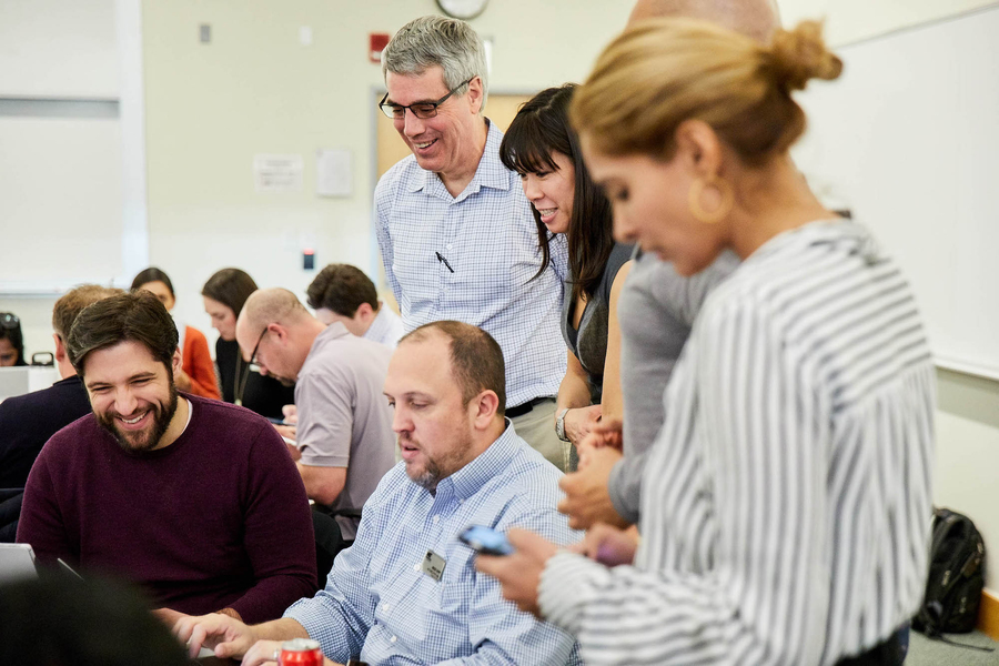 Photo of about 10 people in a classroom, huddled in a cluster, looking at one student's laptop