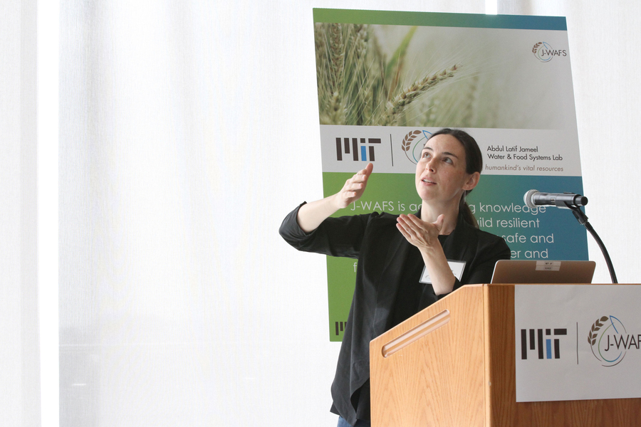 Photo of a woman presenting at a podium, with a poster in the background