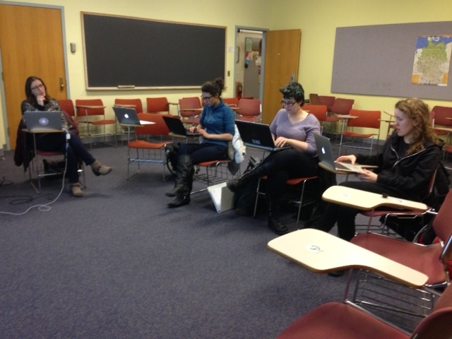 Four women sit in a classroom, working on laptops