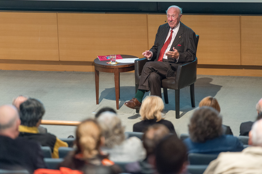 Photo of George Shultz seated, giving a talk in front of an audience in a lecture hall