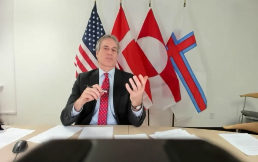 Blurry photo of a man sitting at a desk in front of flags