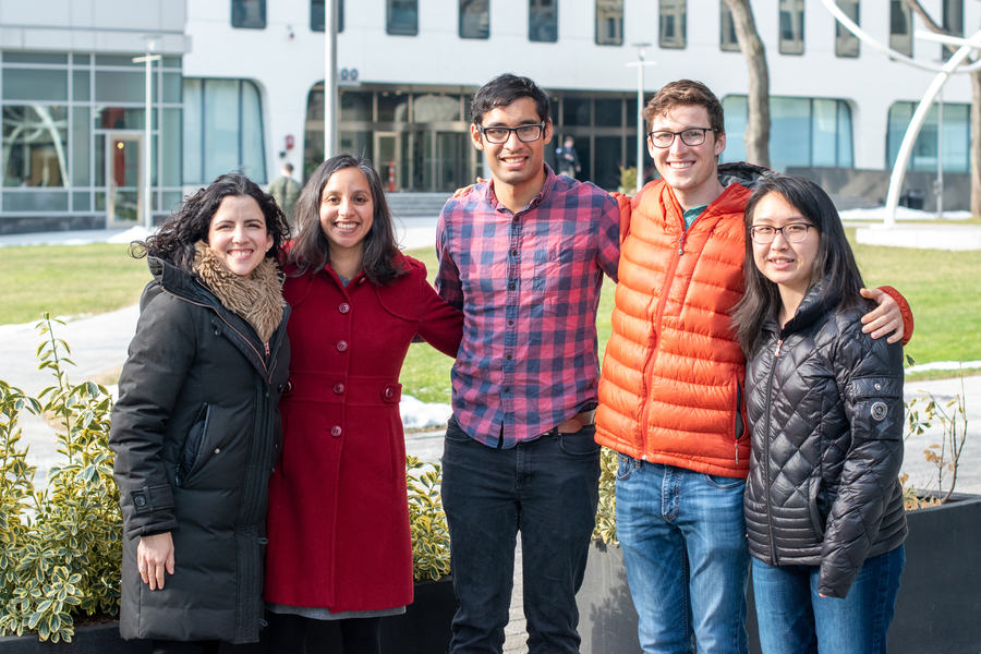 Photo of five people posing with their arms around one another.