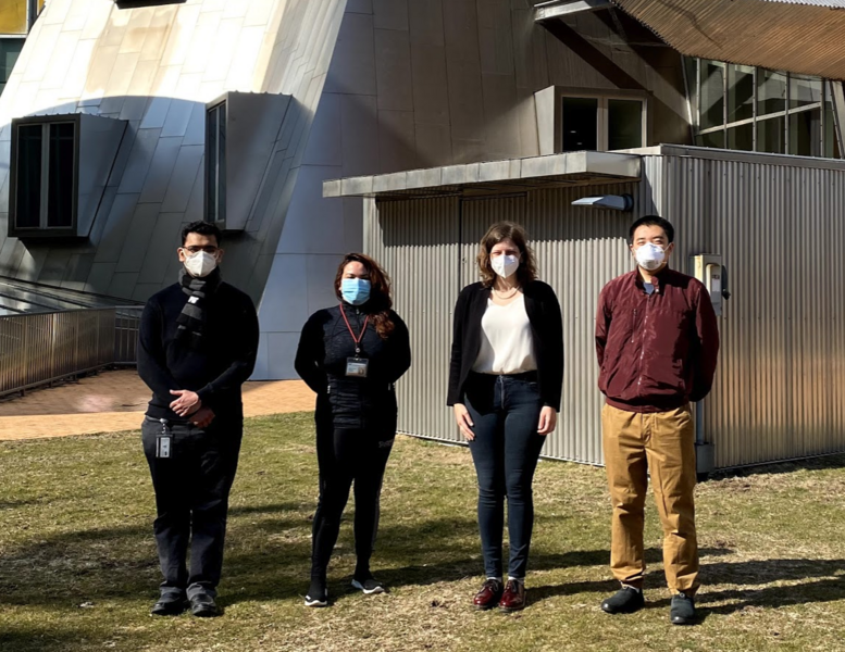 A photo of four people standing outside the Stata Center, wearing facemasks