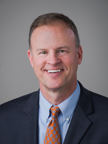 Headshot portrait of Mark Kurz, wearing a suit and tie and smiling at the camera.