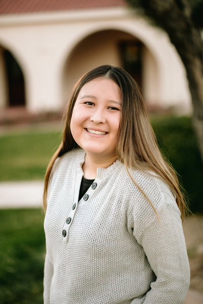 Photo of a young woman smiling at the camera. Her hair is long and she is wearing a cream-colored sweater. 