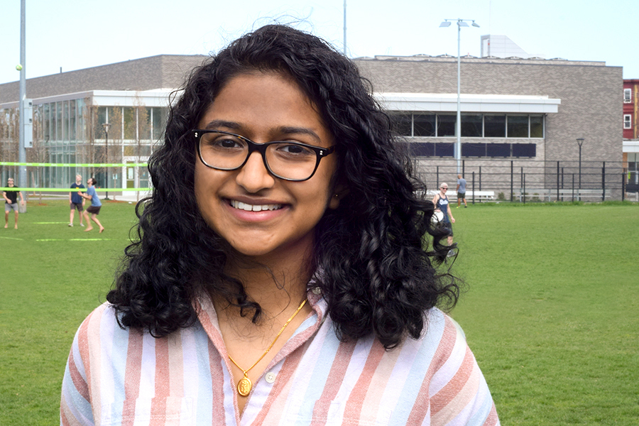 Photo of Anjali Nambrath, smiling and outdoors with an athletic field in the background