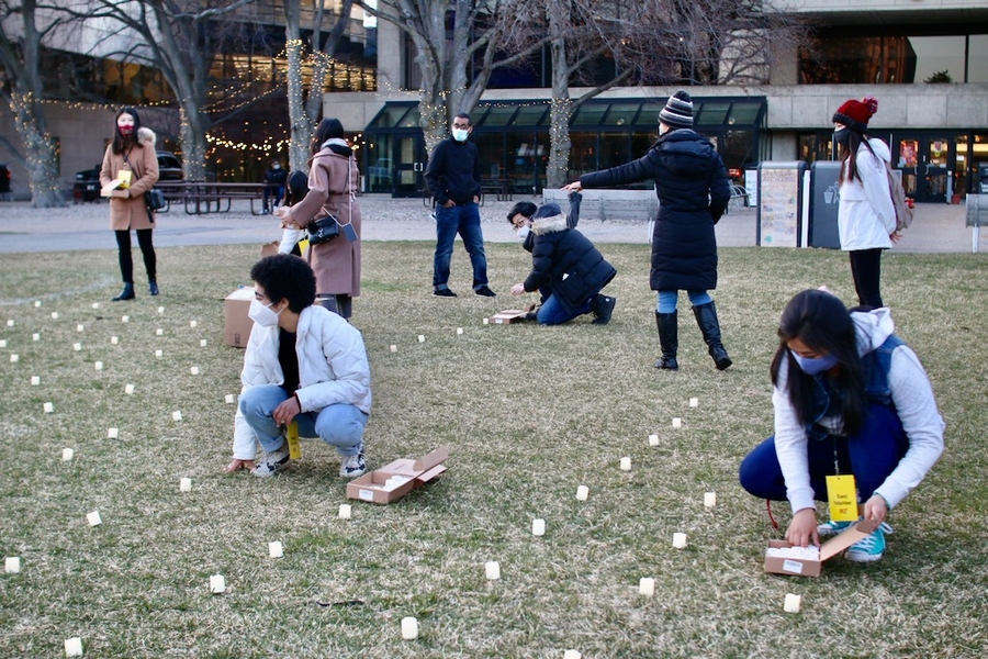 Photo of students gathered on Kresge Oval placing candles on the grass. They are masked and most are wearing winter jackets.