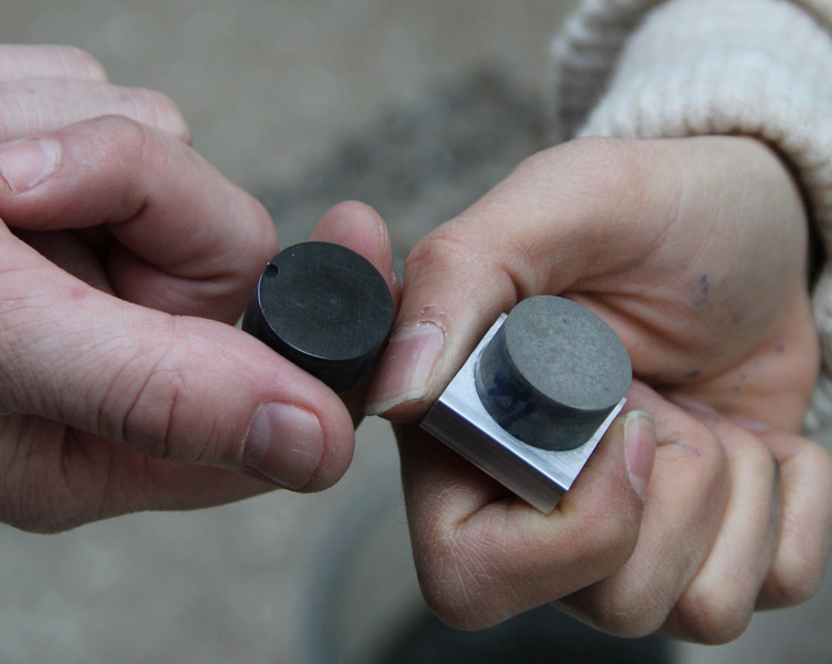 Close-up photo of two people's hands holding cement sample disks.