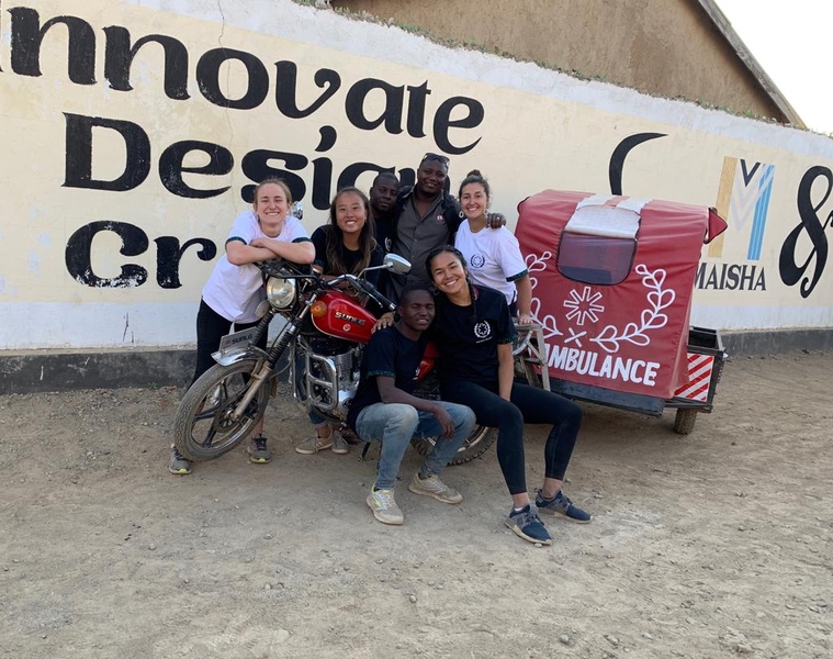 Photo of the Okoa Project team posing around a motorcycle outfitted with an ambulance trailer
