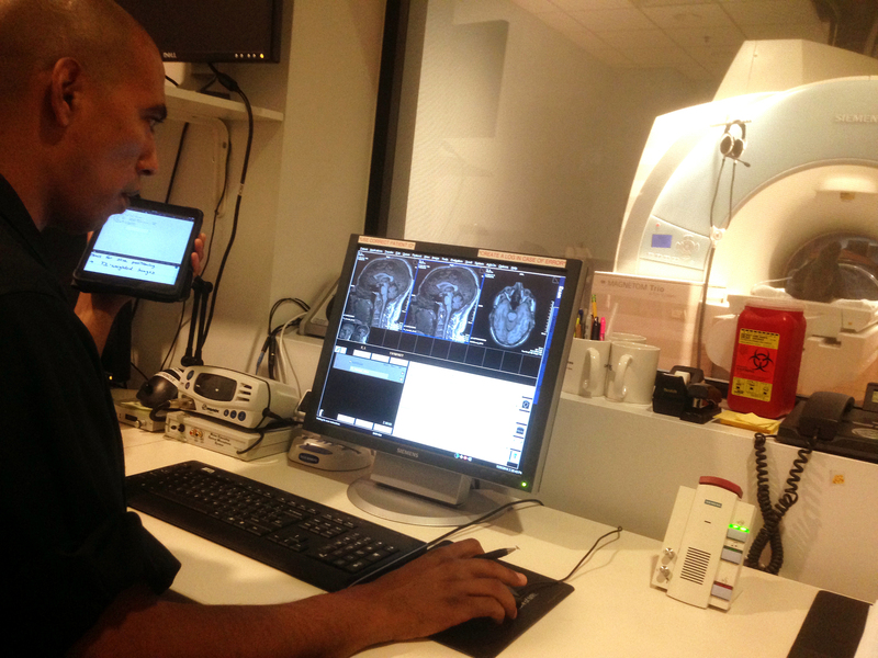 A man seated at a desk looking at scans of a brain on a computer screen
