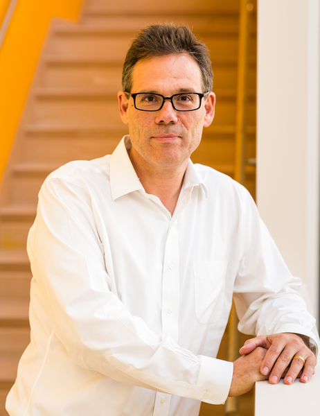 Portrait photo of Michale Fee, standing in front of a staircase and leaning on the banister