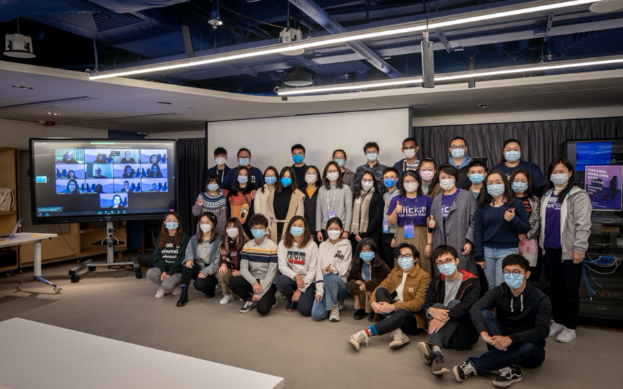 Photo of about 30 students posing at MIT Innovation Node. They are all masked, and 13 more are virtually present on a screen.