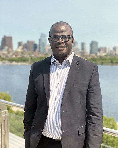 Photo of Carl Dey smiling and standing in front of the Charles River
