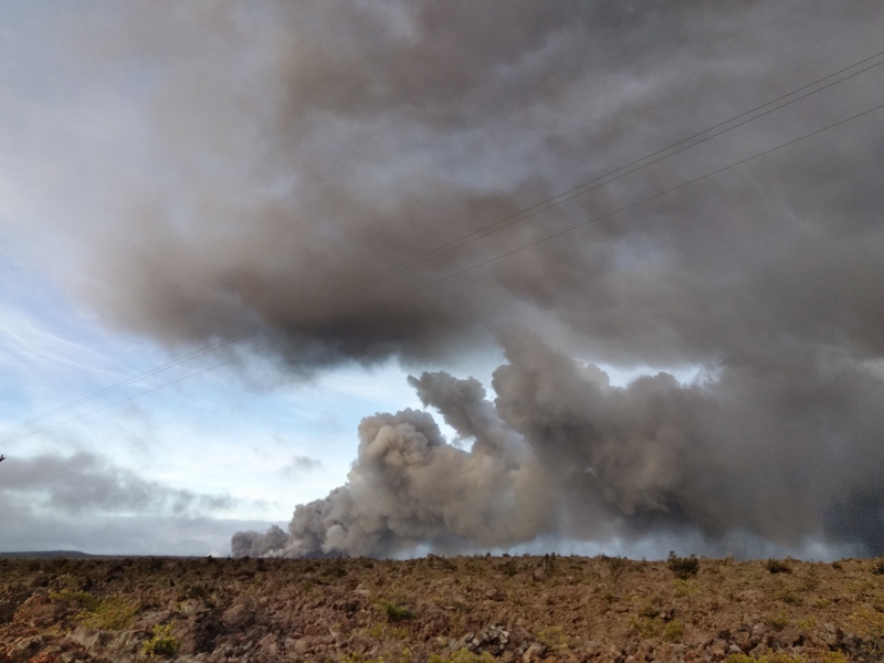 Photo of a plume of volcanic smog rising into the air from a flat plain of mostly dirt and rock