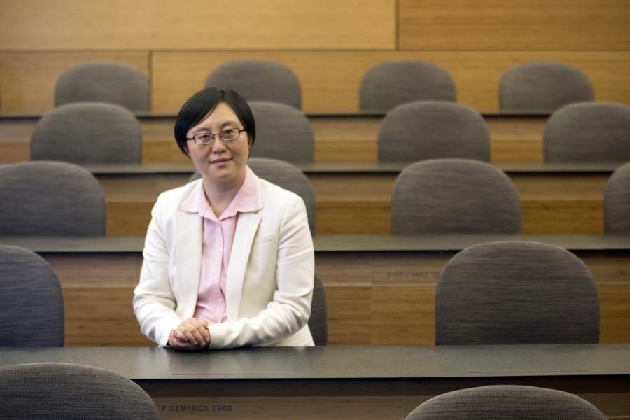 Portrait photo of Siqi Zheng sitting at a long table in an otherwise-empty classroom.