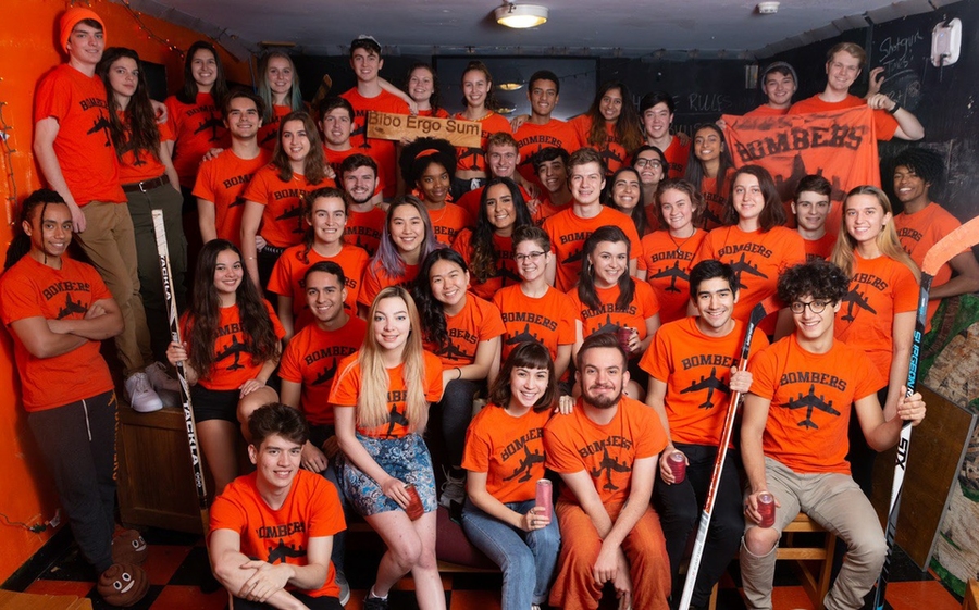 Miles Johnson, in bottom left corner, with a large number of young people all wearing orange t-shirts that feature a simple outline of an airplane and the word "Bombers" on them