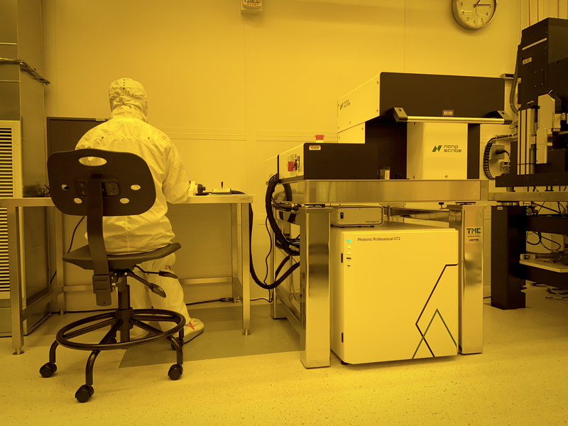 Yellow-tinted photo of a researcher in a clean suit using a large piece of lab equipment
