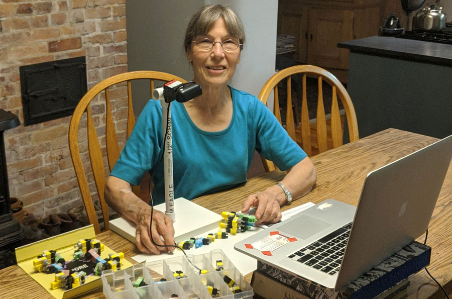Photo of Kathy Vandiver sitting at a dining room table with her plastic models and an open laptop facing her